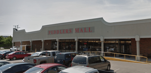 Exterior view of Peddlers Mall with a parking lot filled with cars under a clear sky.