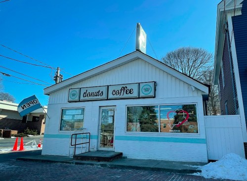 A small, white building with a sign reading "donuts coffee" and a heart-shaped decoration in the window.