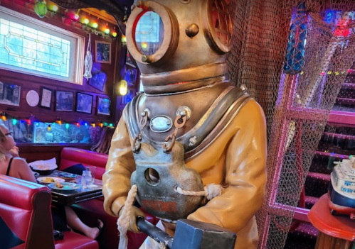 A vintage diver statue stands in a colorful restaurant, surrounded by nautical decor and dim lighting.