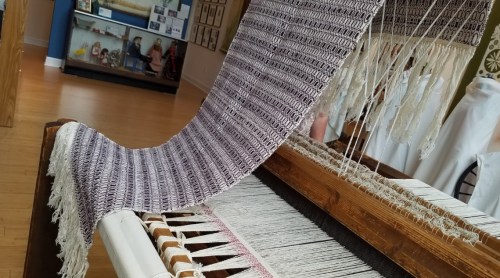 A close-up of a weaving loom with a patterned textile in progress, showcasing intricate threads and textures.