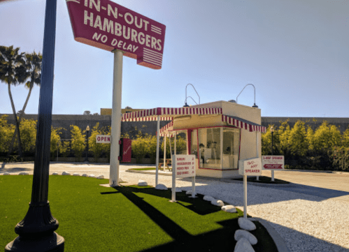 A retro-style In-N-Out Burger stand with a red and white sign, surrounded by green grass and white rocks.