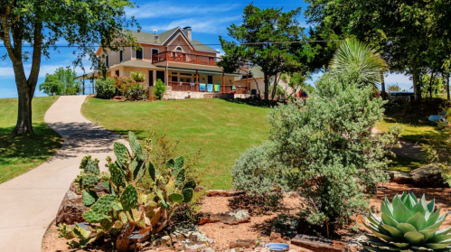 A large house on a hill surrounded by greenery and cacti, with a clear blue sky above.