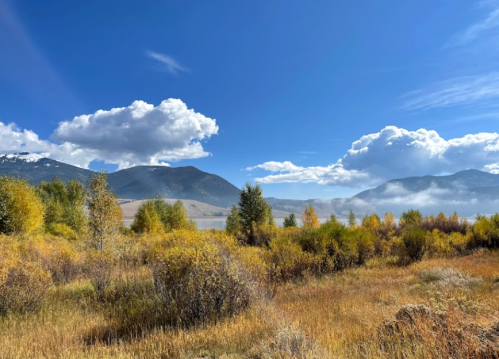 A scenic landscape featuring mountains, fluffy clouds, and autumn foliage in vibrant yellow and green hues.
