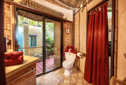 Cozy bathroom with bamboo accents, red curtains, and a view of a lush outdoor area through glass doors.