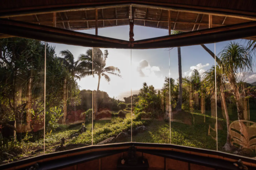 A scenic view through a large window, showcasing lush greenery and palm trees against a sunset sky.