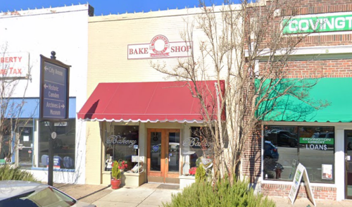 A quaint bake shop with a red awning, surrounded by other storefronts in a small town.