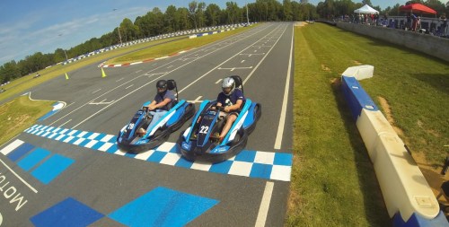 Two go-karts race side by side on a track, approaching the finish line marked by blue and white checkered patterns.