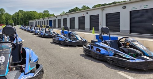 A row of blue go-karts parked in front of storage units on a sunny day.