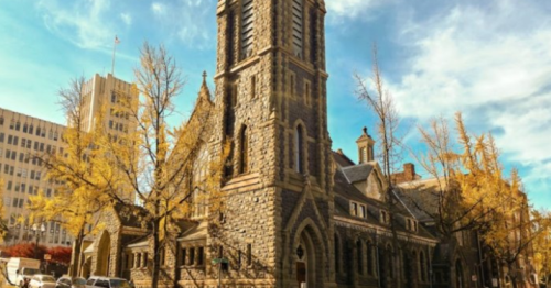 Historic stone church with a tall tower, surrounded by autumn trees and a clear blue sky.
