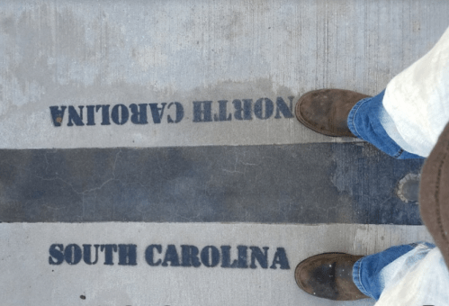Feet standing on a concrete line marking the border between North Carolina and South Carolina.