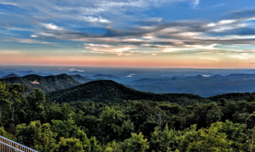 A panoramic view of rolling green mountains under a colorful sunset sky.