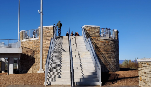 A stone structure with stairs leading up, people sitting on top, and a clear blue sky in the background.