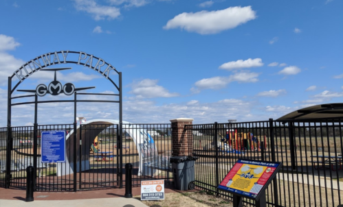 Entrance to Runway Park with a playground visible in the background and a blue sky with clouds above.