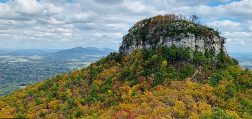 A scenic view of a rocky mountain surrounded by vibrant autumn foliage under a cloudy sky.