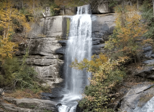 A cascading waterfall flows over rocky cliffs, surrounded by vibrant autumn foliage.