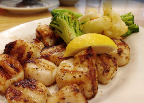 Grilled shrimp with lemon and a side of steamed broccoli and cauliflower on a white plate.