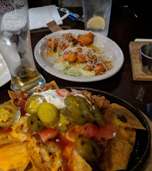 A plate of loaded nachos with jalapeños, tomatoes, and sour cream, alongside a plate of shrimp and salad.