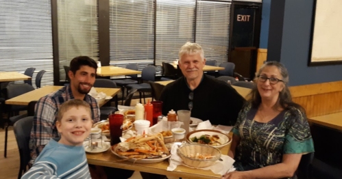 A family of four enjoys a meal at a restaurant, with plates of food and drinks on the table.