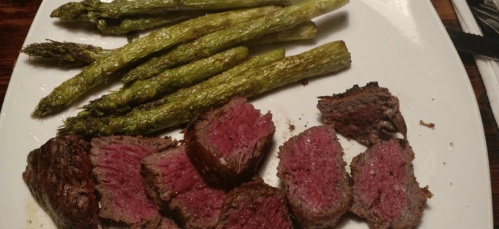 A plate with sliced medium-rare steak and roasted asparagus spears.