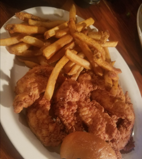 A plate of crispy fried chicken strips served with golden French fries and a soft bun.