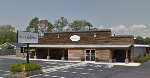 Exterior of Shay's Steakhouse, featuring a wooden facade and a sign, with a parking lot and greenery in front.