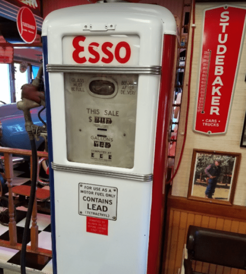 Vintage Esso gas pump with a red and white design, displaying price and fuel information, in a retro-themed setting.