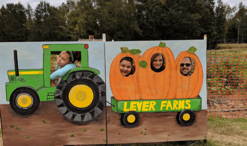 A colorful farm-themed cutout featuring a tractor and pumpkins, with four people posing through the holes.