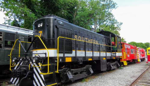 A black and yellow Southern Railway locomotive parked beside a red caboose in a green, wooded area.