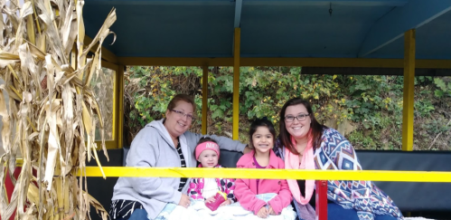 Four people, including two children, sit together on a colorful train, surrounded by autumn foliage.