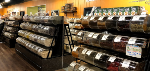A spice shop with shelves of clear containers filled with various spices and herbs, labeled for easy identification.