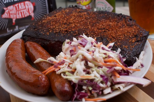 A plate featuring a large piece of smoked brisket, two sausages, and a side of coleslaw.