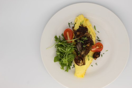 A plate featuring a fluffy omelette topped with mushrooms, cherry tomatoes, and fresh greens.