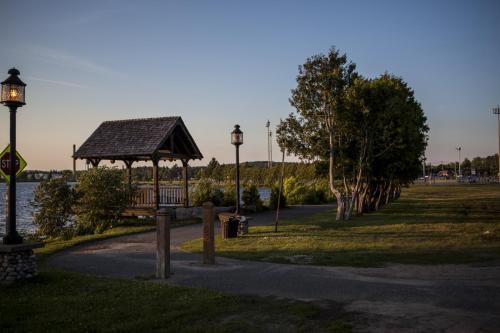 A peaceful waterfront scene featuring a gazebo, trees, and a pathway along the water at sunset.