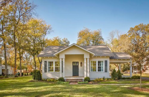 A charming white house with a front porch, surrounded by green grass and trees under a clear blue sky.