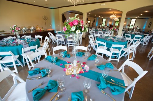 Elegant event space with teal and gray table settings, floral centerpieces, and white chairs arranged for a celebration.
