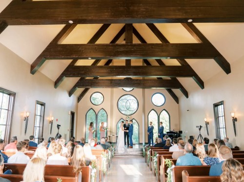 A wedding ceremony in a rustic chapel with wooden beams, guests seated, and a couple exchanging vows.