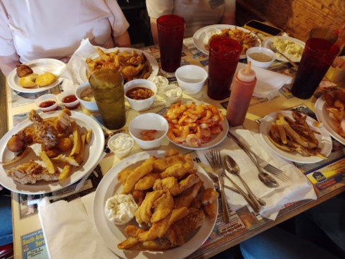A table filled with various plates of fried seafood, fries, sauces, and drinks in a casual dining setting.