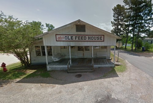 A rustic building with a sign reading "Abe's Ole Feed House," featuring a porch and surrounded by trees.