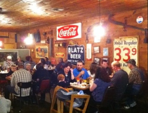 A busy restaurant interior with diners at tables, vintage signs on the walls, and a warm, rustic atmosphere.