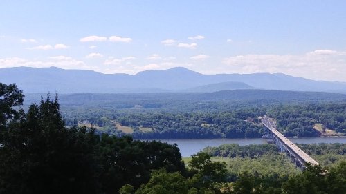 A scenic view of a river winding through green hills, with mountains in the background under a clear blue sky.