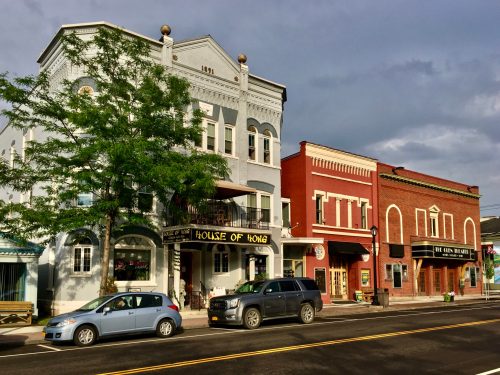 A street view featuring two colorful buildings: a blue restaurant and a red brick shop, with parked cars and trees.