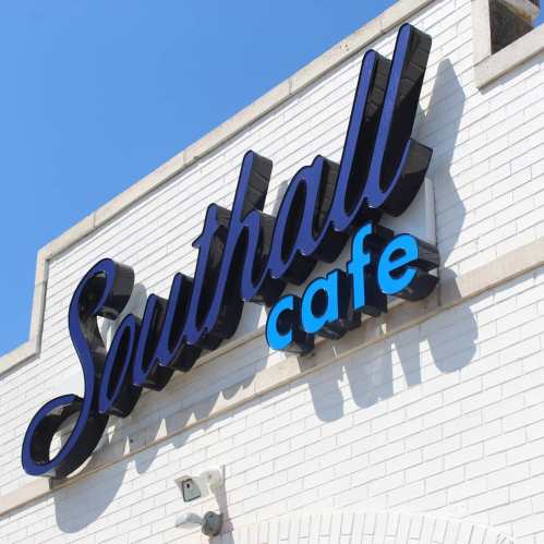 Sign for Southall Cafe against a clear blue sky, featuring bold lettering in dark blue and light blue.