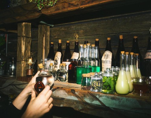 A wooden shelf filled with various glass bottles and jars containing colorful liquids and herbs.
