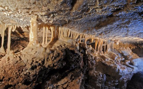 Stalactites and stalagmites in a dimly lit cave, showcasing unique rock formations and textures.