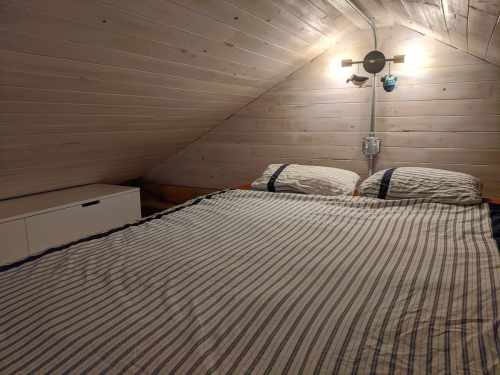 Cozy attic bedroom with a sloped wooden ceiling, a double bed, and a minimalist nightstand.
