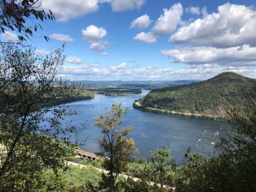 A scenic view of a river winding through green hills under a blue sky with fluffy clouds.