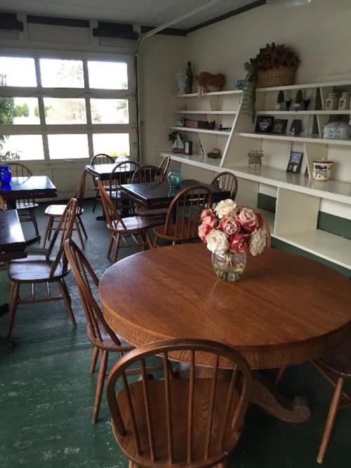 A cozy room with wooden tables and chairs, featuring a vase of flowers on a round table and shelves in the background.