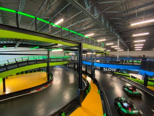 Indoor go-kart track with multiple levels, featuring bright green and yellow accents and a winding black racing surface.