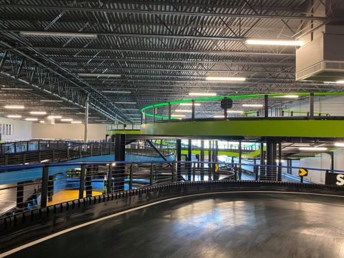 Indoor go-kart track featuring multiple levels, sleek black surfaces, and vibrant green and blue accents.