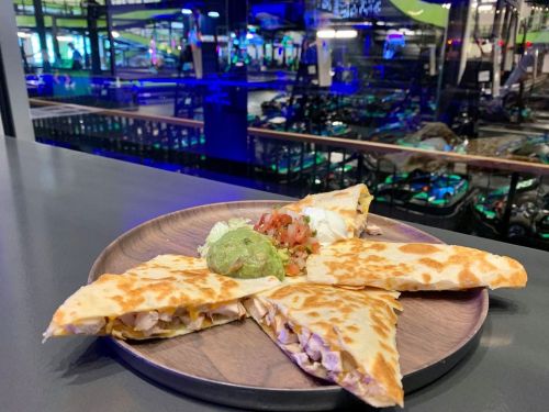 A wooden plate with quesadillas, guacamole, and salsa, set against a colorful, illuminated background.